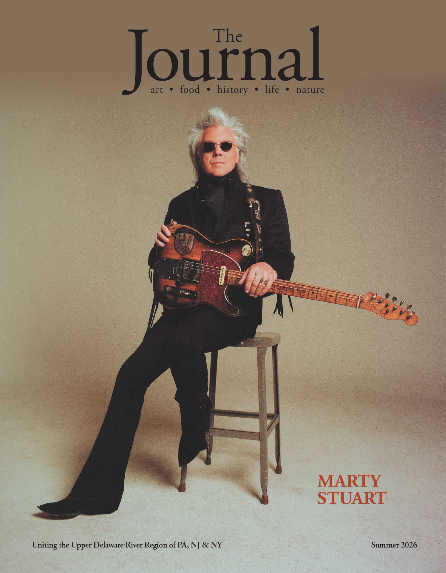 Marty Stuart with a guitar sitting on a stool